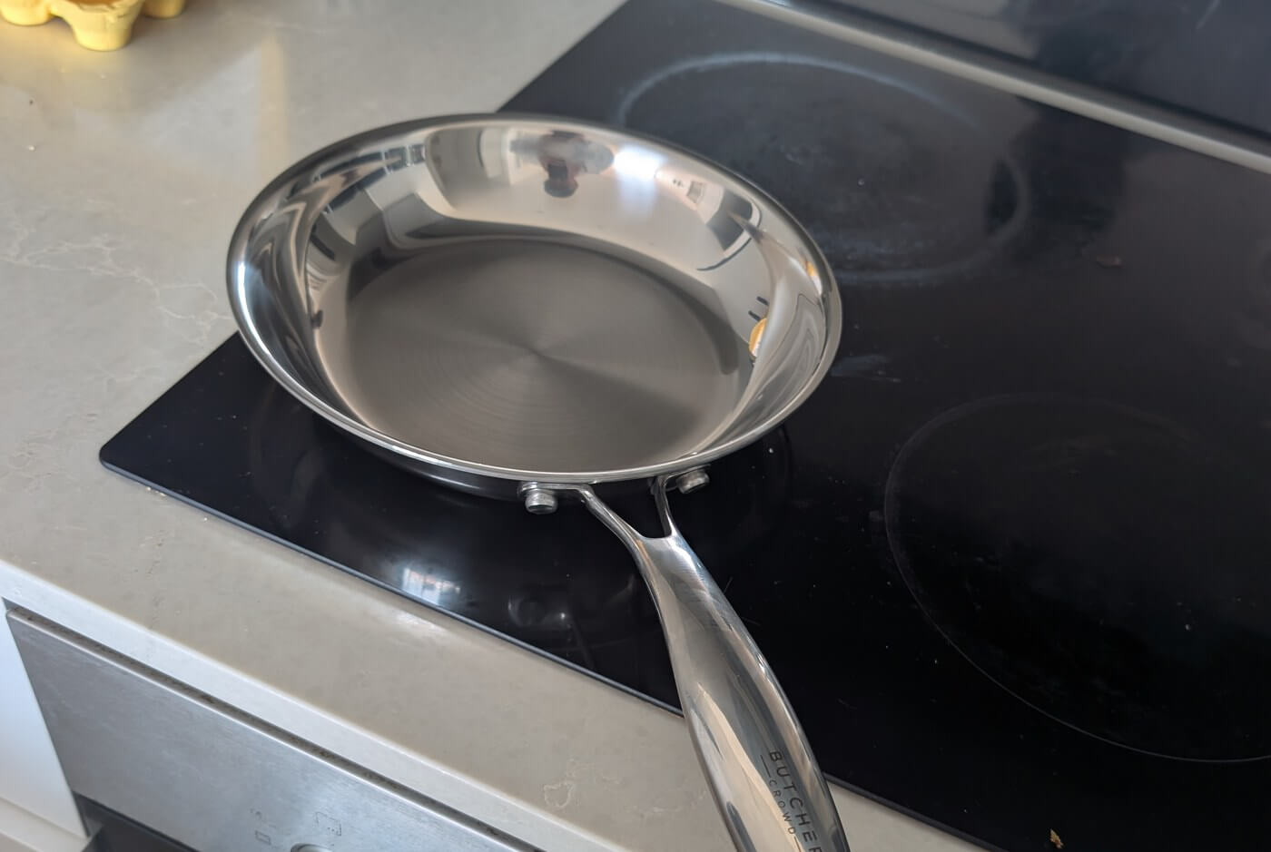 The ButcherCrowd stainless steel frying pan sitting on an induction cooktop in a home kitchen