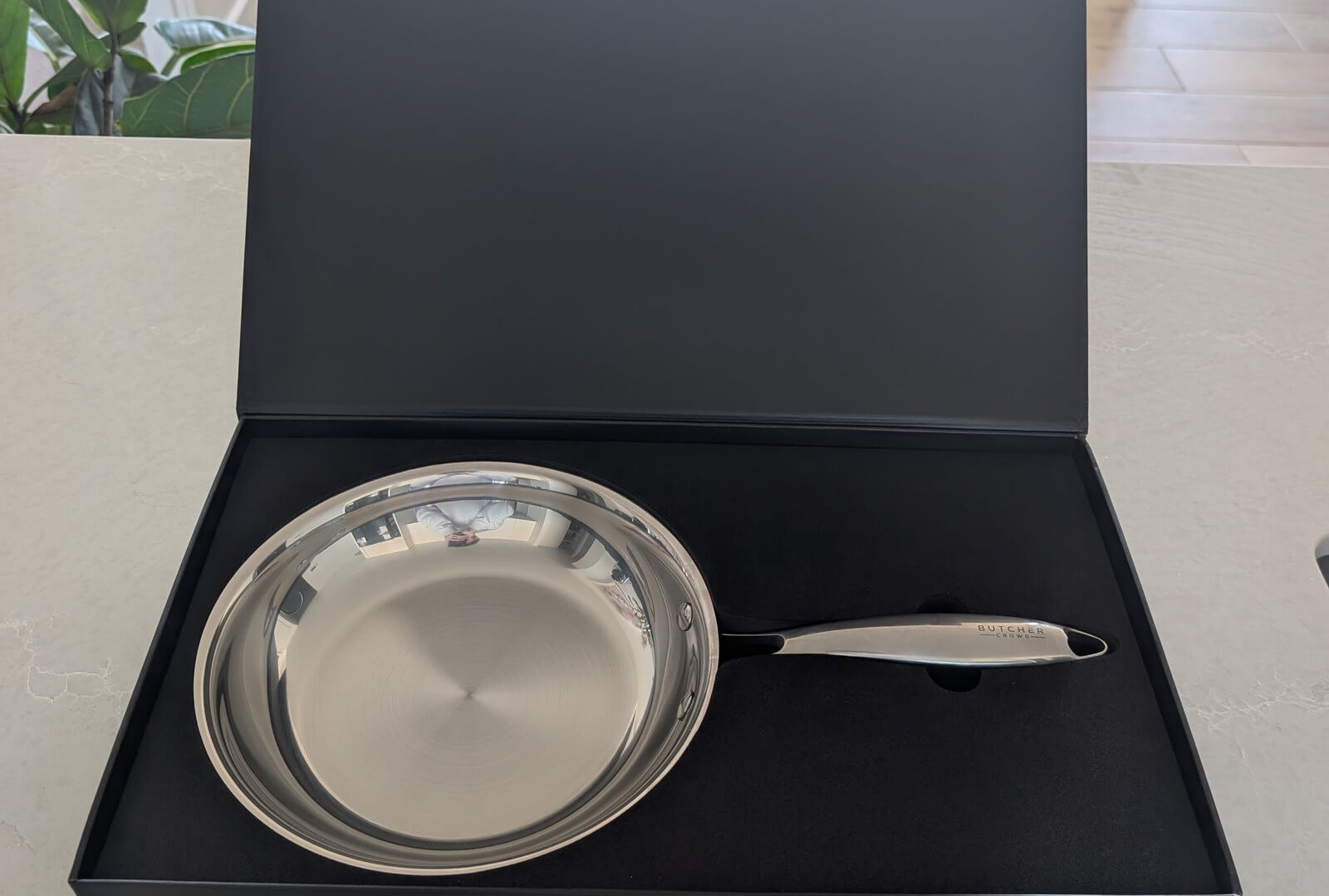 The ButcherCrowd stainless steel frying pan and its handle presented in an open black magnetic display box on a kitchen benchtop